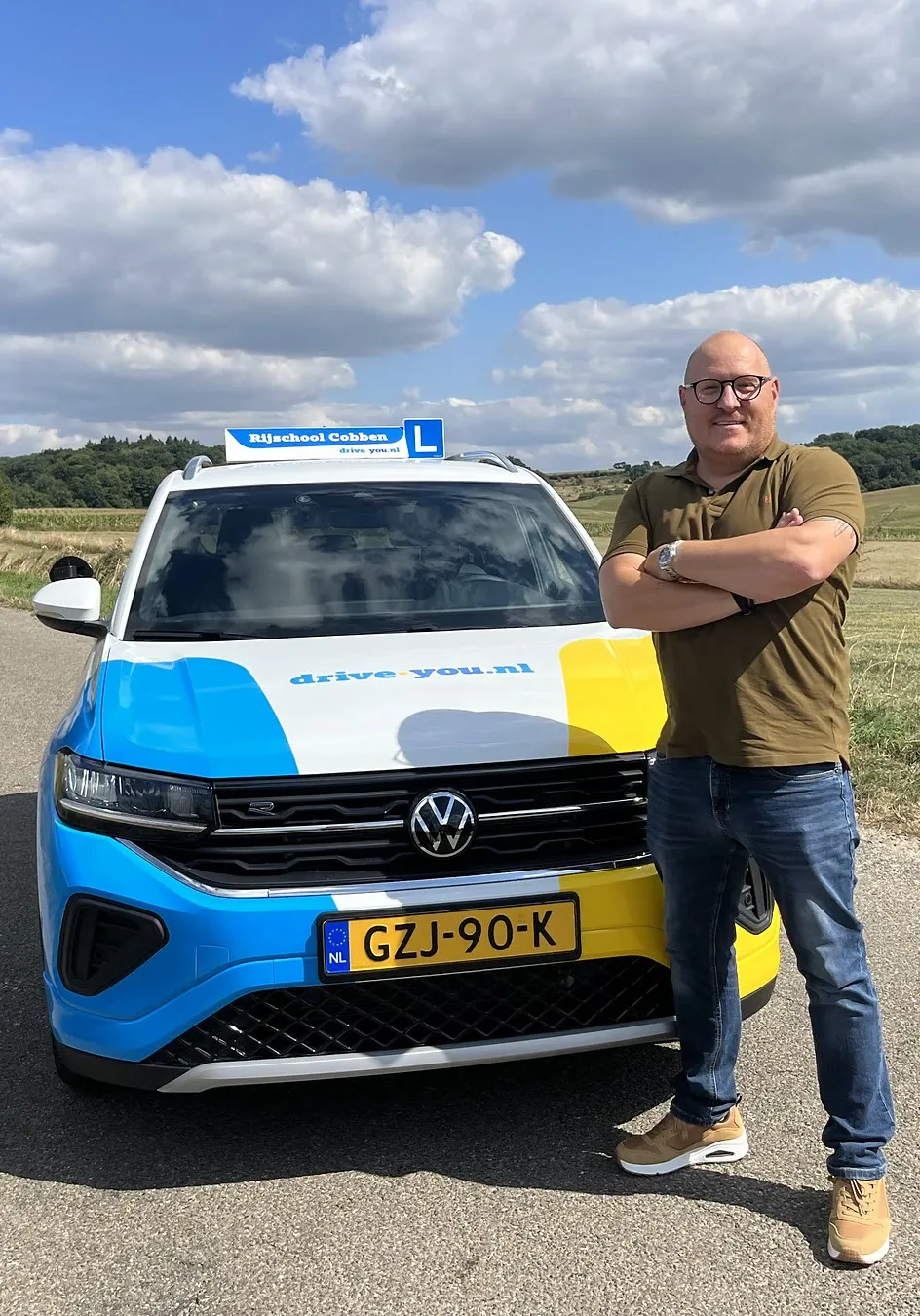 Niels Cobben met zijn armen over elkaar bij de lesauto op een landweg in het Zuid-Limburgse heuvelland